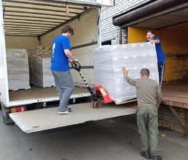 Рабочие загружают палету с упакованным грузом в грузовой автомобиль.