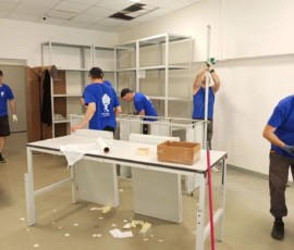 Сотрудники собирают металлические стеллажи и рабочую мебель в помещении.