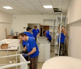 Несколько сотрудников одновременно собирают мебель и стеллажи в рабочем помещении.