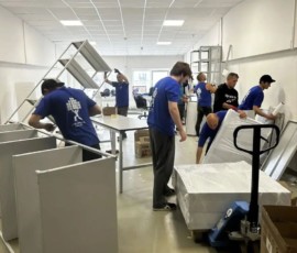 Группа сотрудников разбирает и перемещает мебель в большом помещении.
